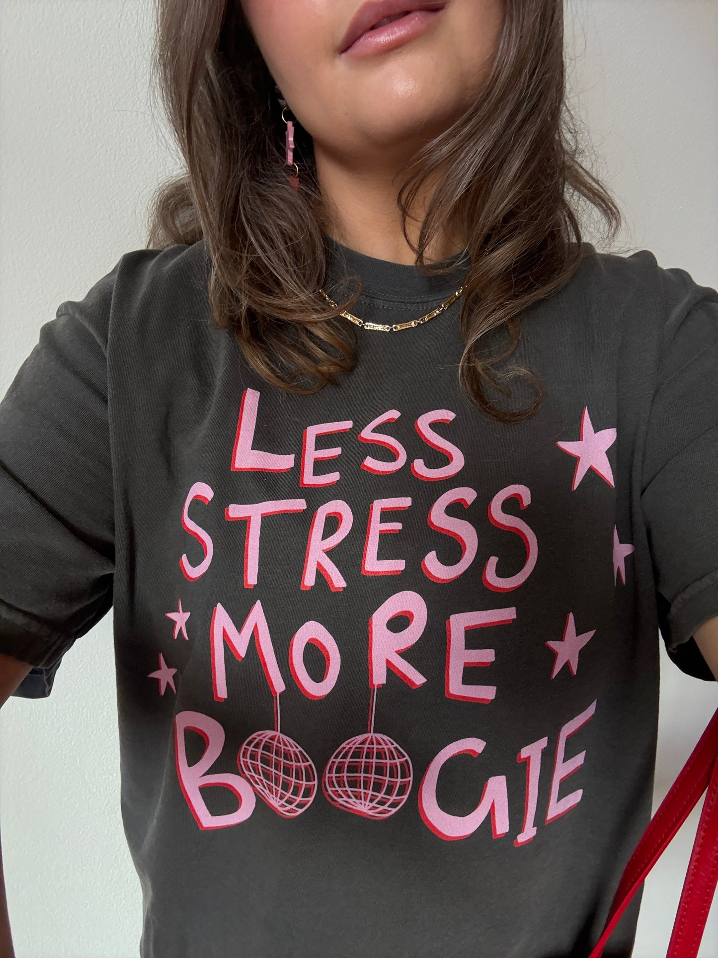 Person wearing a black t-shirt with pink text 'LESS STRESS MORE BOOGIE' on a plain background