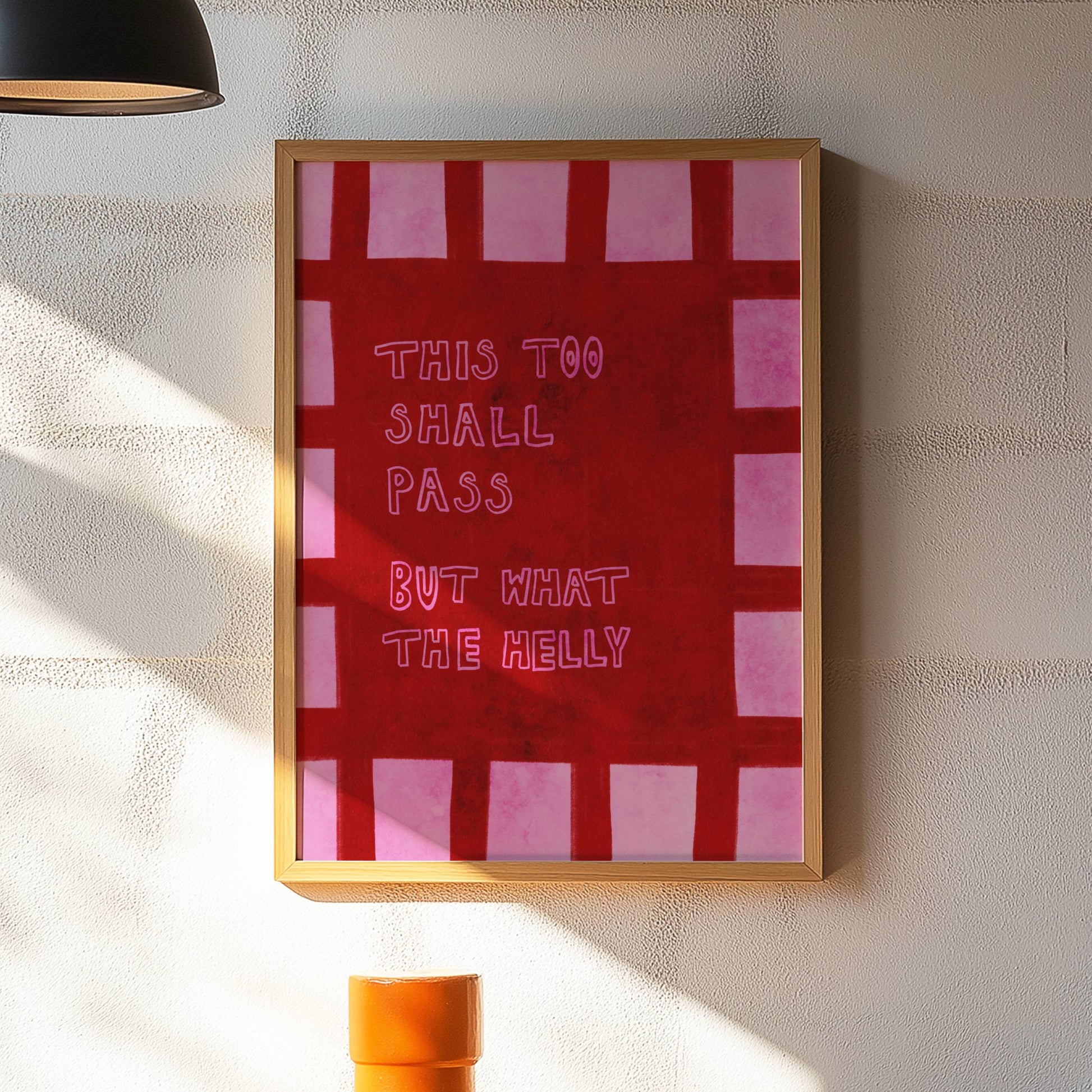 Framed artwork with text on a wall in a room with a lamp and table.